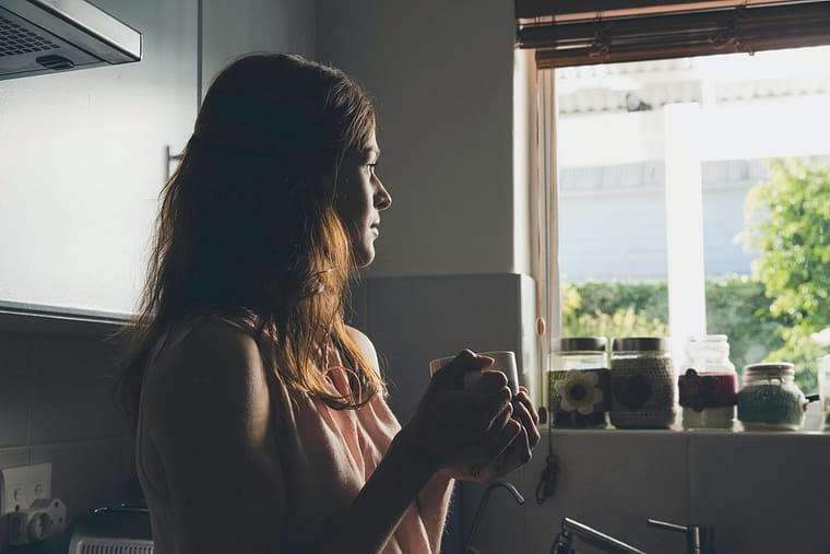 Young woman having a coffee break gazing through kitchen window