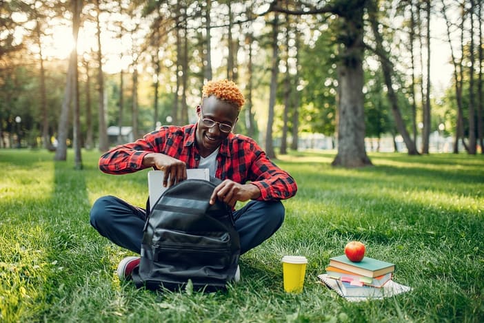 Black student with backpack sitting on the grass