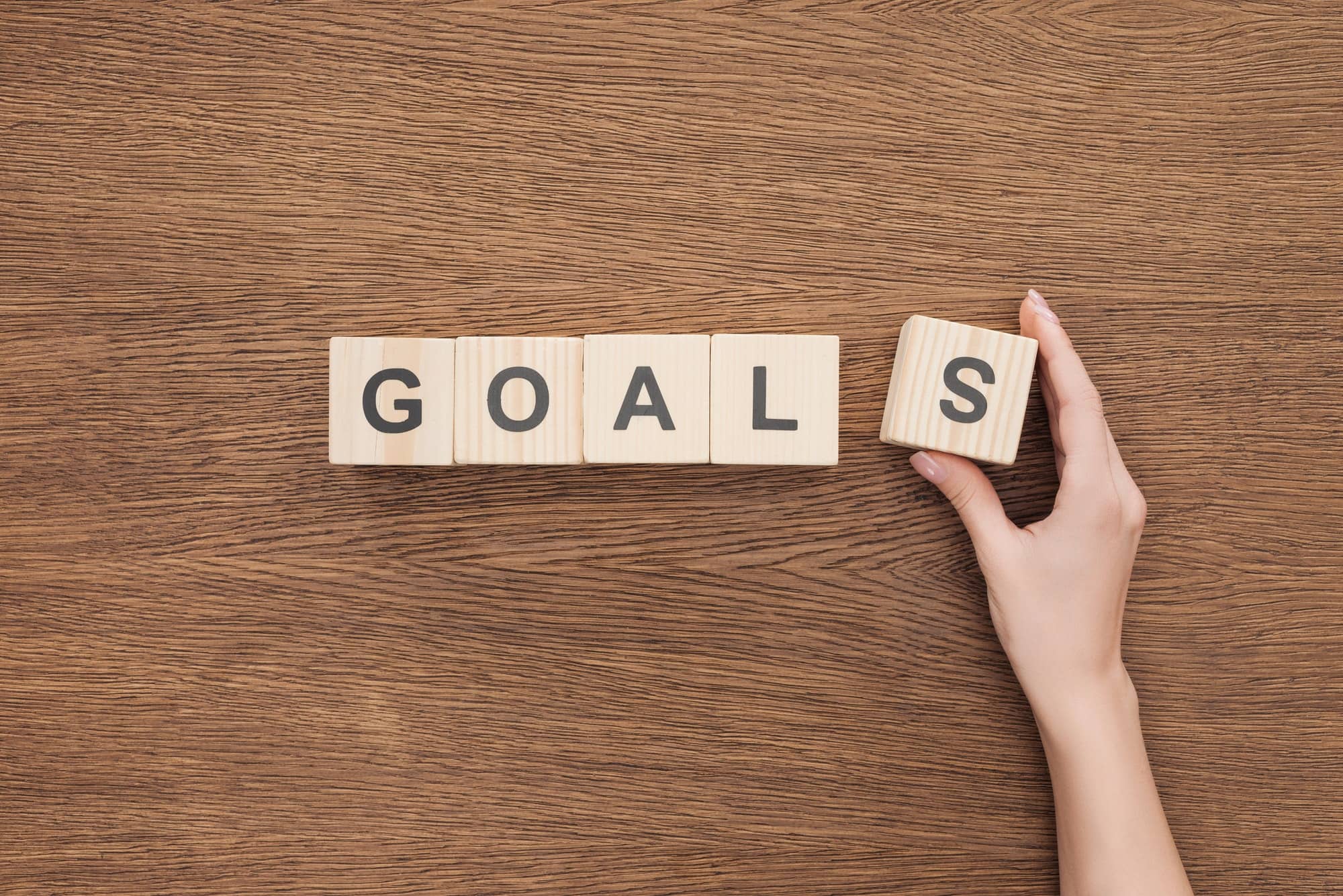 cropped view of person adjusting 'goals' word made of wooden blocks on wooden tabletop, goal setting