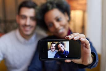 Mixed race couple making selfie with phone in cafe